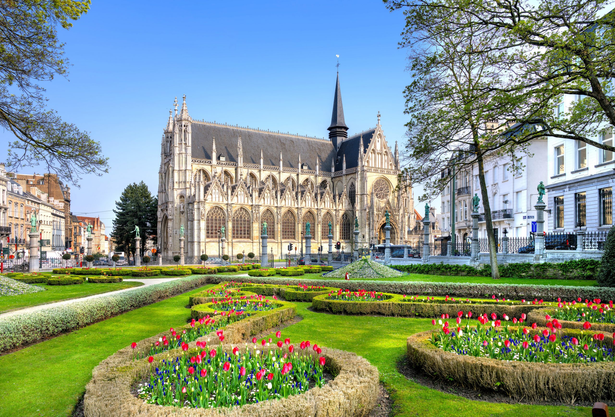 NIKON CORPORATION Vue extérieure de l'église Notre-Dame au Sablon à Bruxelles, entourée de jardins avec des parterres de fleurs et des statues sur des colonnes.