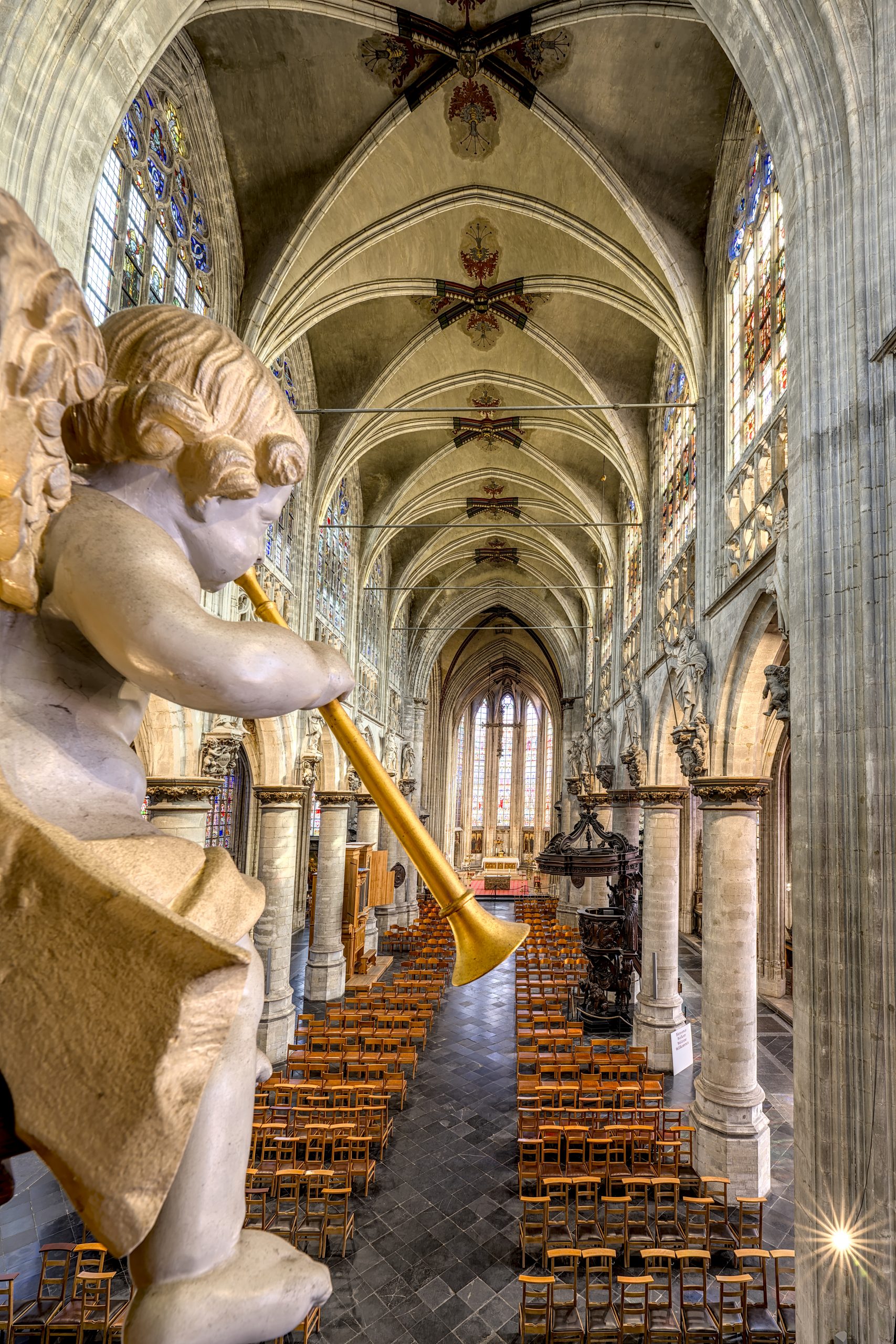 Binnenaanzicht van de kerk Notre-Dame au Sablon met een cherubijn die een trompet vasthoudt op de voorgrond en rijen stoelen op de achtergrond.