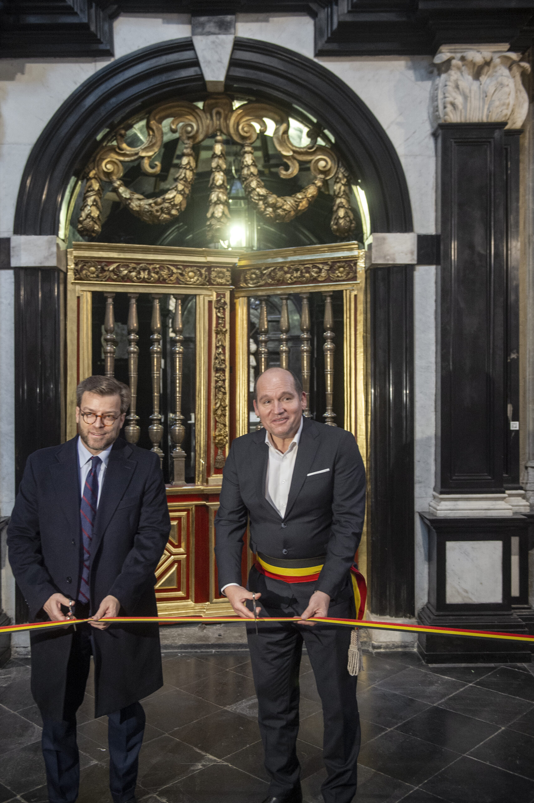 Twee mannen knippen een lint door voor een sierlijke deur na de restauratie van de kapel van Sint Ursula.